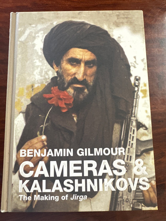 Book cover of 'Cameras & Kalashnikovs' by Benjamin Gilmour on a wooden surface