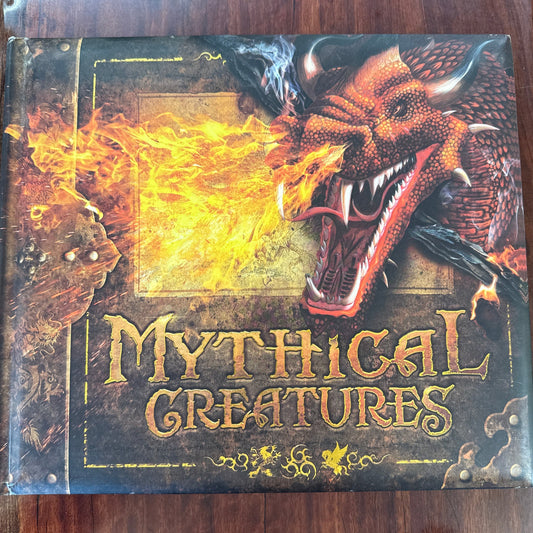 Book titled 'Mythical Creatures' with a dragon illustration on a wooden surface