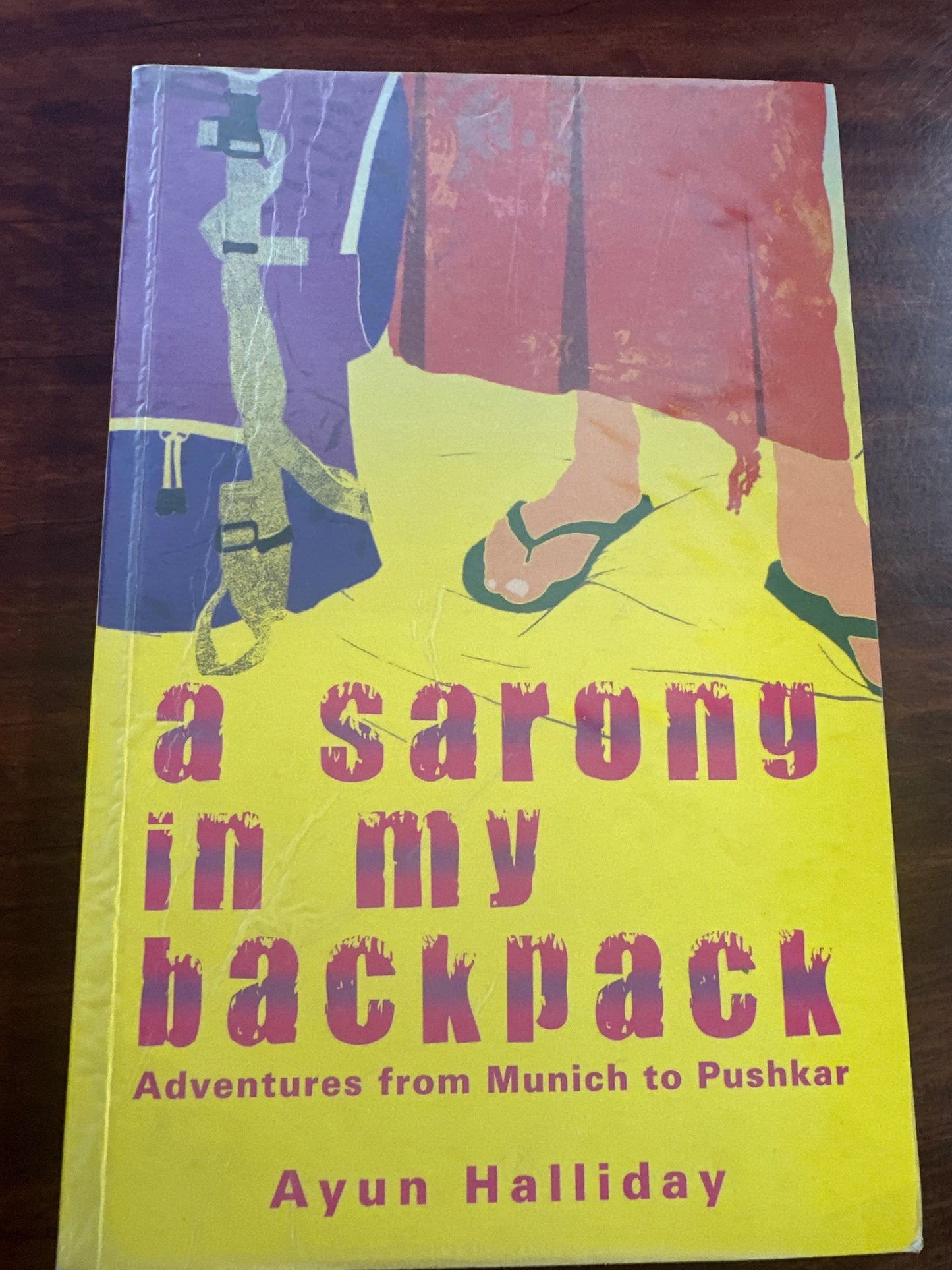 Book cover of 'A Sarong in My Backpack' by Ayun Halliday on a wooden surface