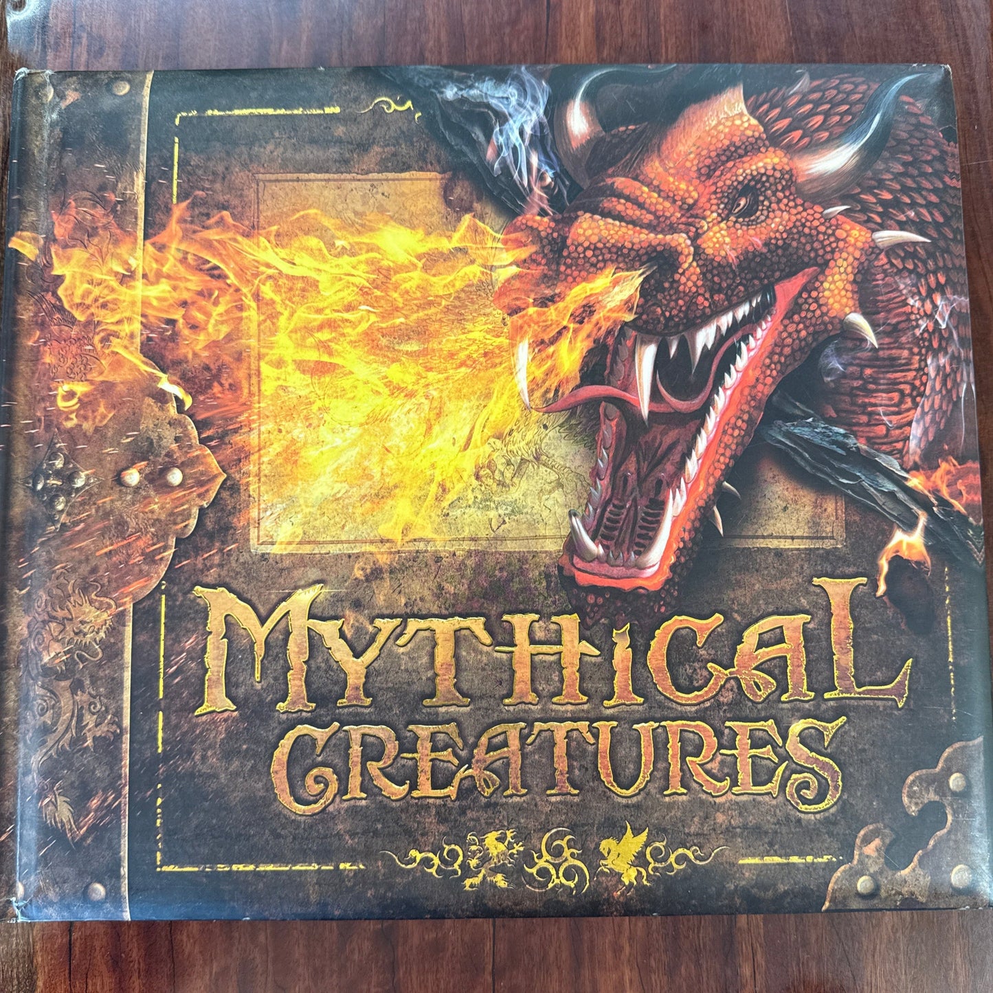 Book titled 'Mythical Creatures' with a dragon illustration on a wooden surface