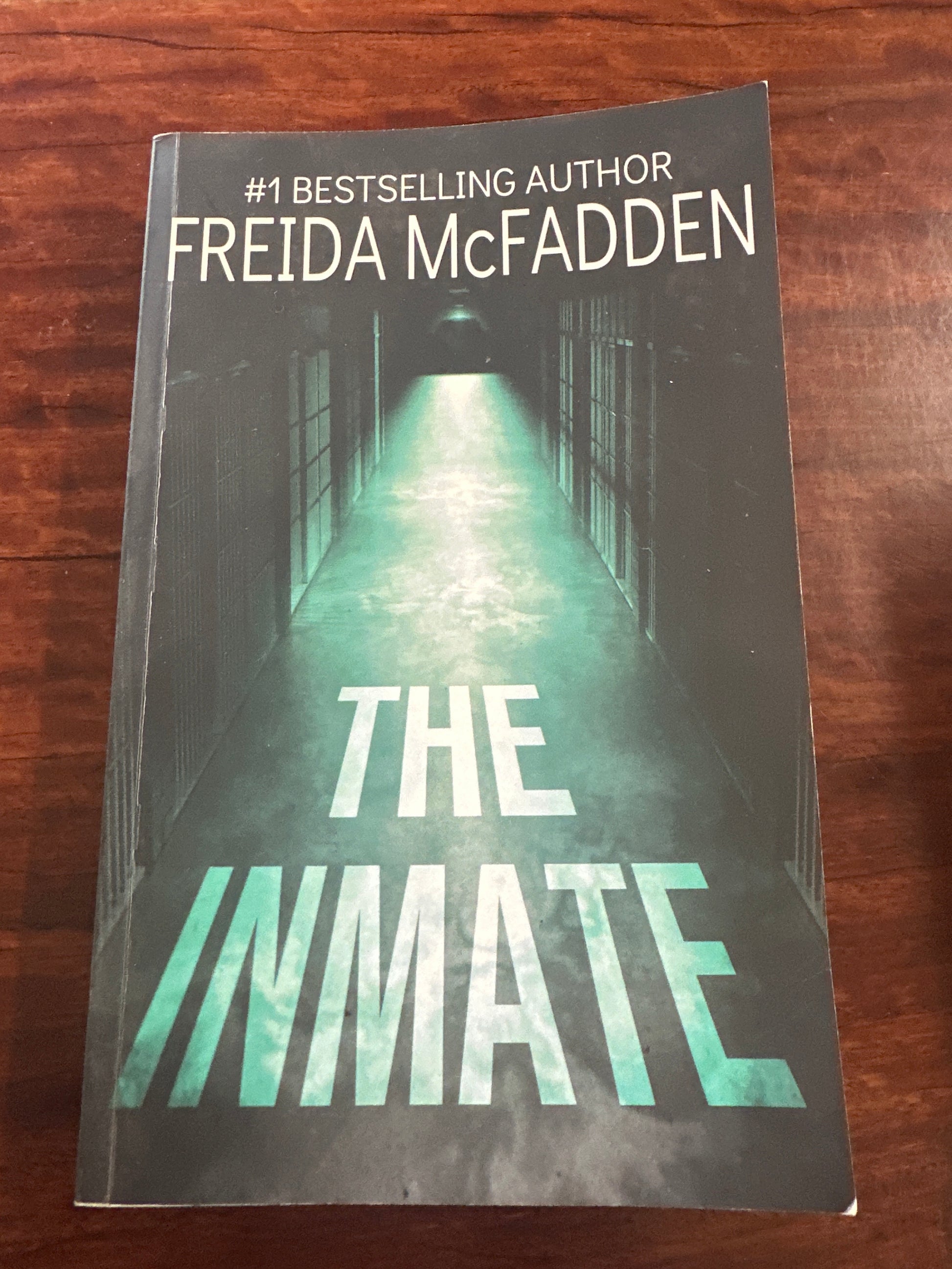 Book titled 'The Inmate' by Freida McFadden on a wooden surface