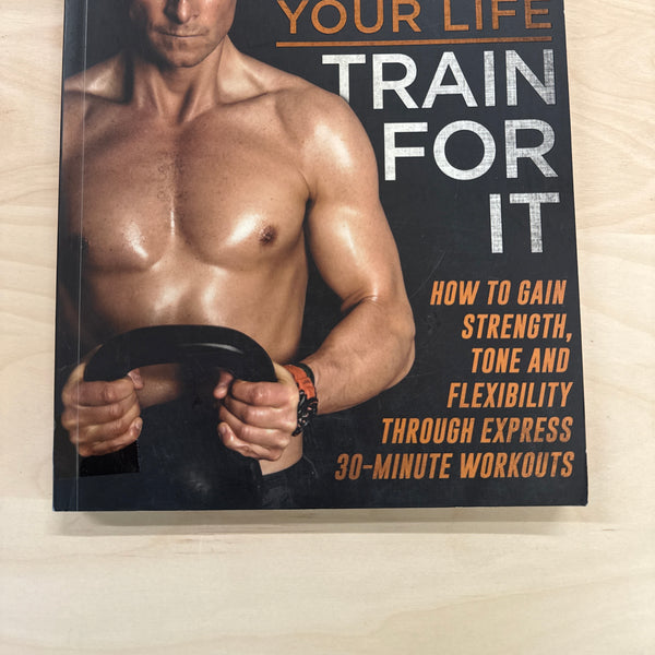 Book titled 'Train For It' by Bear Grylls on a wooden surface