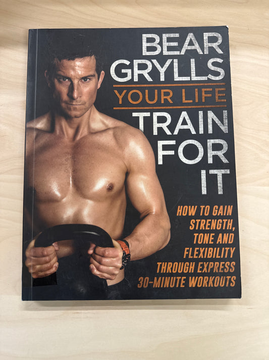 Book titled 'Train For It' by Bear Grylls on a wooden surface